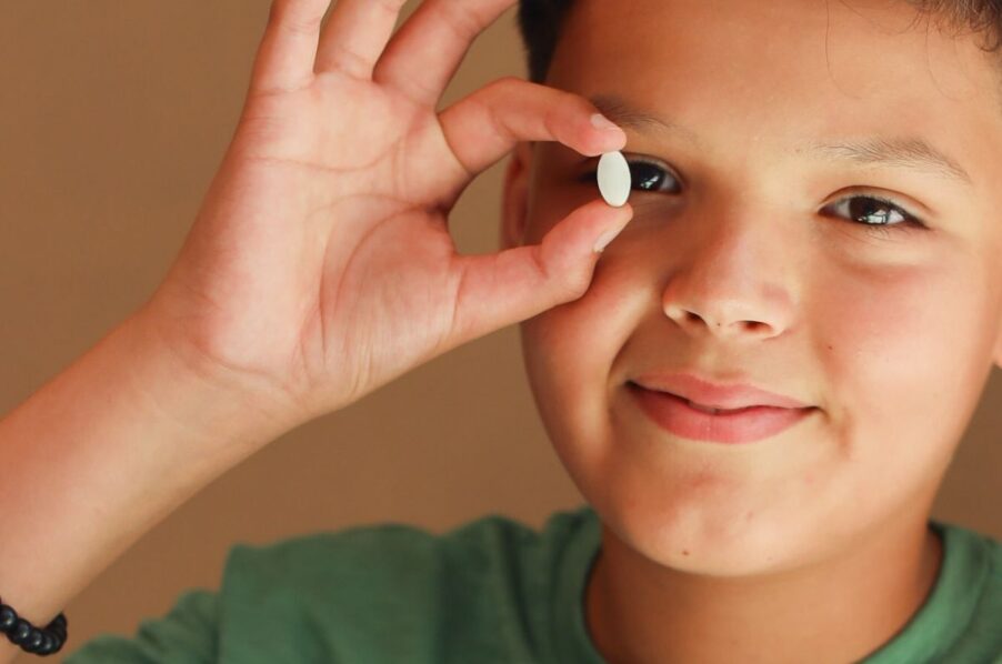 Glimlachende jongen in een groen T-shirt houdt een witte kauwtablet speels voor zijn oog.