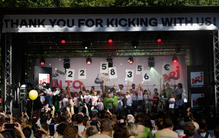 The final donation amount revealed on stage at RUN TO KICK 2025, surrounded by children and participants celebrating KickCancer’s solidarity race.