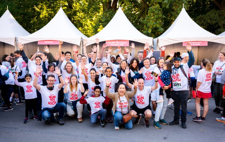 Une équipe corporate de participants portant des T-shirts RUN TO KICK pose ensemble, les mains levées, lors de la course solidaire de KickCancer.