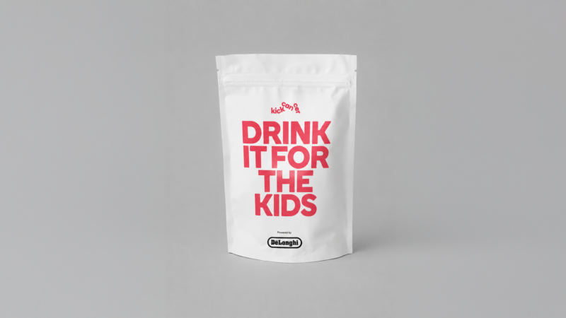 White coffee pouch with the red KickCancer logo and the words DRINK IT FOR THE KIDS in large red letters, with the De'Longhi logo and the line Powered by De'Longhi at the bottom.