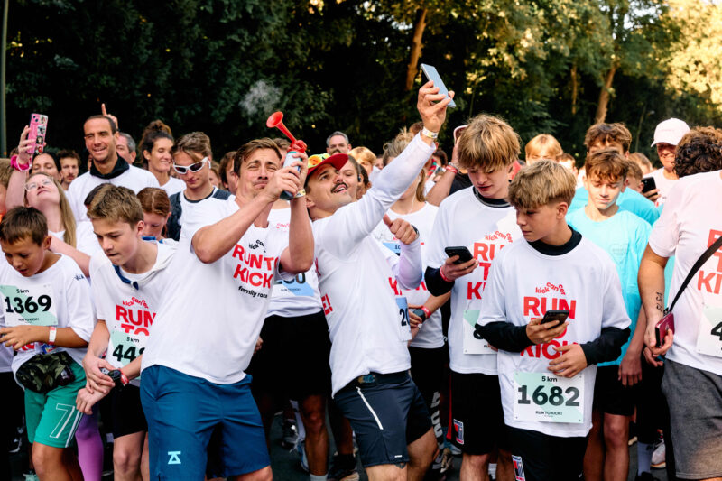 Des participants portant des T-shirts RUN TO KICK se rassemblent sur la ligne de départ tandis que les ambassadeurs Niels Destadsbader et Average Rob donnent le coup d’envoi de la course solidaire de KickCancer.