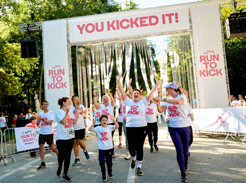 Des participants portant des T-shirts RUN TO KICK célèbrent leur arrivée en franchissant la ligne d’arrivée sous une bannière « YOU KICKED IT! » lors de la course solidaire de KickCancer.