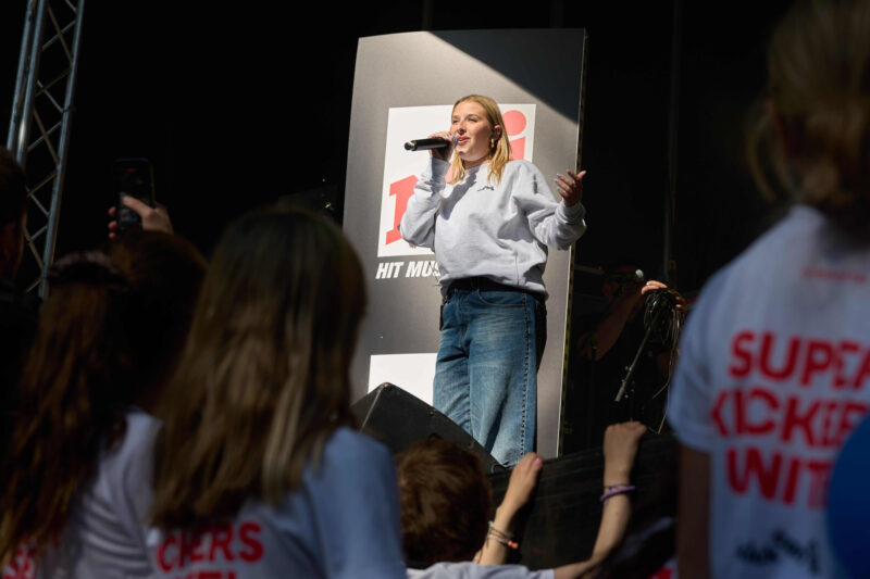 La chanteuse Hélena se produit sur scène lors de RUN TO KICK, tenant un micro devant un public enthousiaste pendant l’événement solidaire de KickCancer.