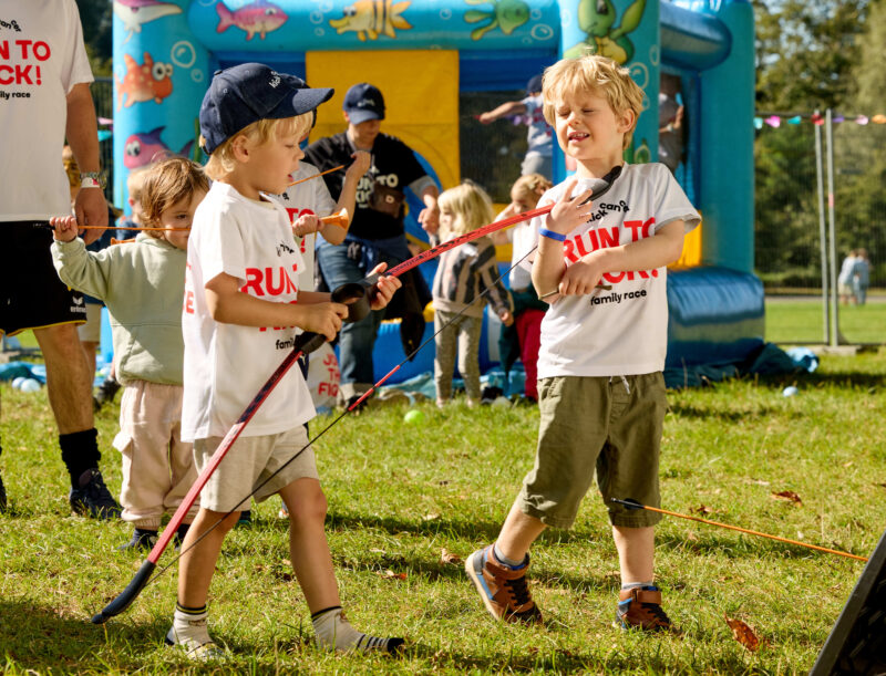 Des enfants portant des T-shirts RUN TO KICK jouent avec des arcs et des flèches près d’un château gonflable lors de l’événement solidaire de KickCancer.