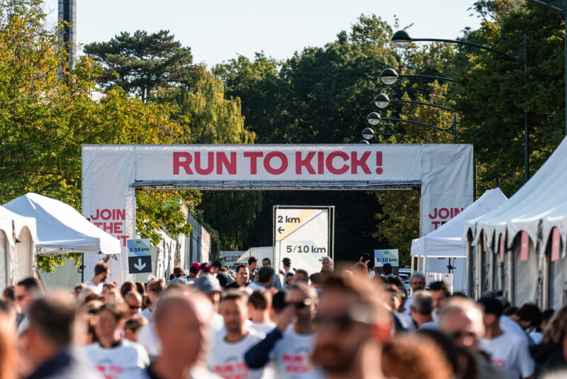 Des participants se rassemblent sous l’arche de départ RUN TO KICK, avec des panneaux indiquant les parcours de 2 km, 5 km et 10 km lors de la course solidaire de KickCancer.