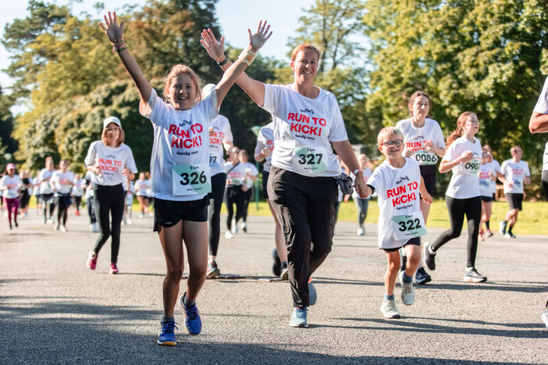 Des enfants et un parent portant des T-shirts RUN TO KICK courent ensemble, main dans la main et souriants lors de la course solidaire de KickCancer.