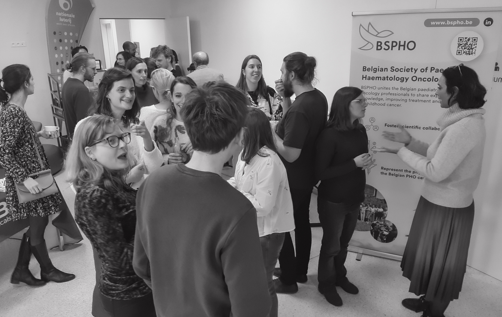 Delphine Heenen speaking with attendees during a BSPHO meeting, surrounded by healthcare professionals and families in a lively networking setting.
