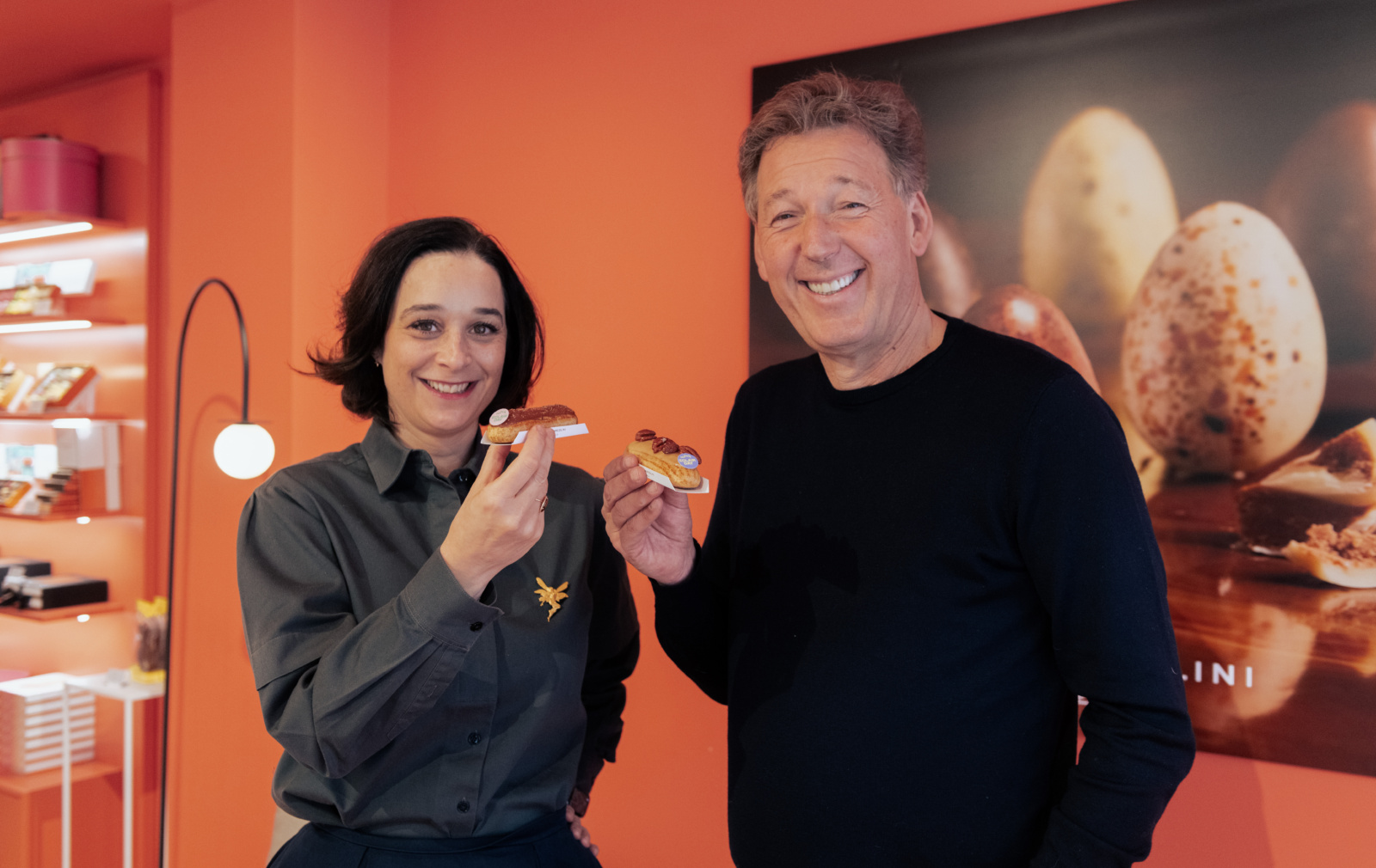 Delphine Heenen et le chocolatier Pierre Marcolini sourient en tenant des éclairs Eclair Day dans la boutique Marcolini.